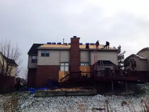 Home improvement project showing workers replacing a roof on a residential house, with scaffolding and equipment visible, emphasizing the use of skilled labor and modern techniques.