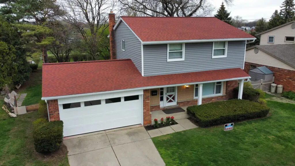 Two-story home with new gray siding and red roof, manicured lawn, and garage, showcasing curb appeal and potential value increase for Southeast Michigan homeowners.