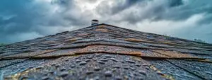 a close-up view of a residential roof in bloomfield hills, showcasing visible wear and damage such as missing shingles and water stains, with a dramatic sky overhead that highlights the urgency of needed repairs.